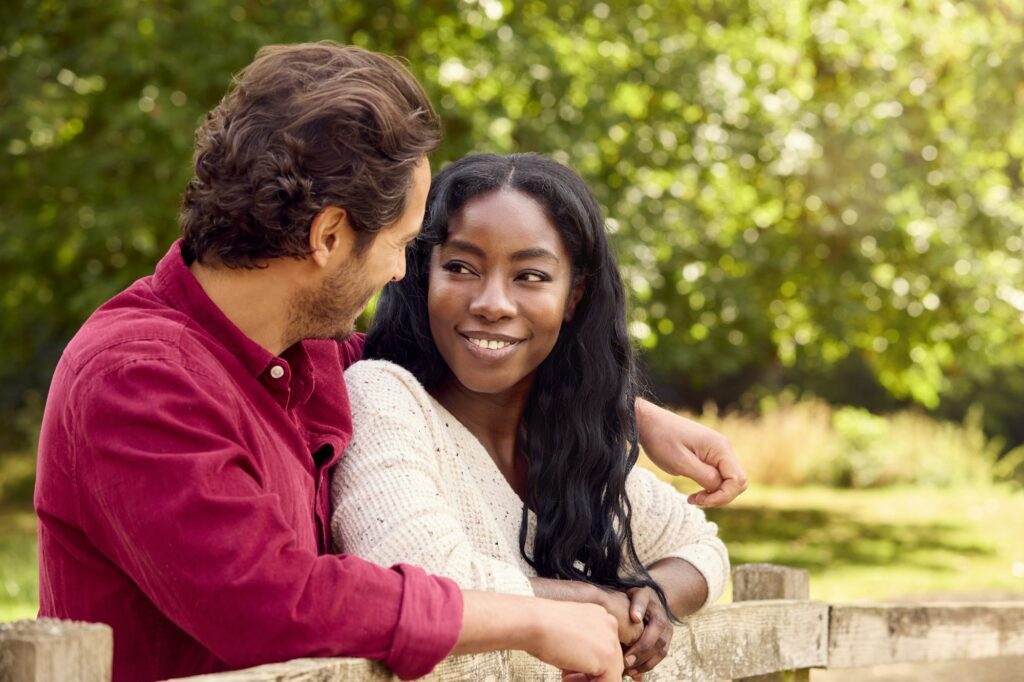 Loving Mixed Race Couple Leaning On Fence On Walk In Countryside